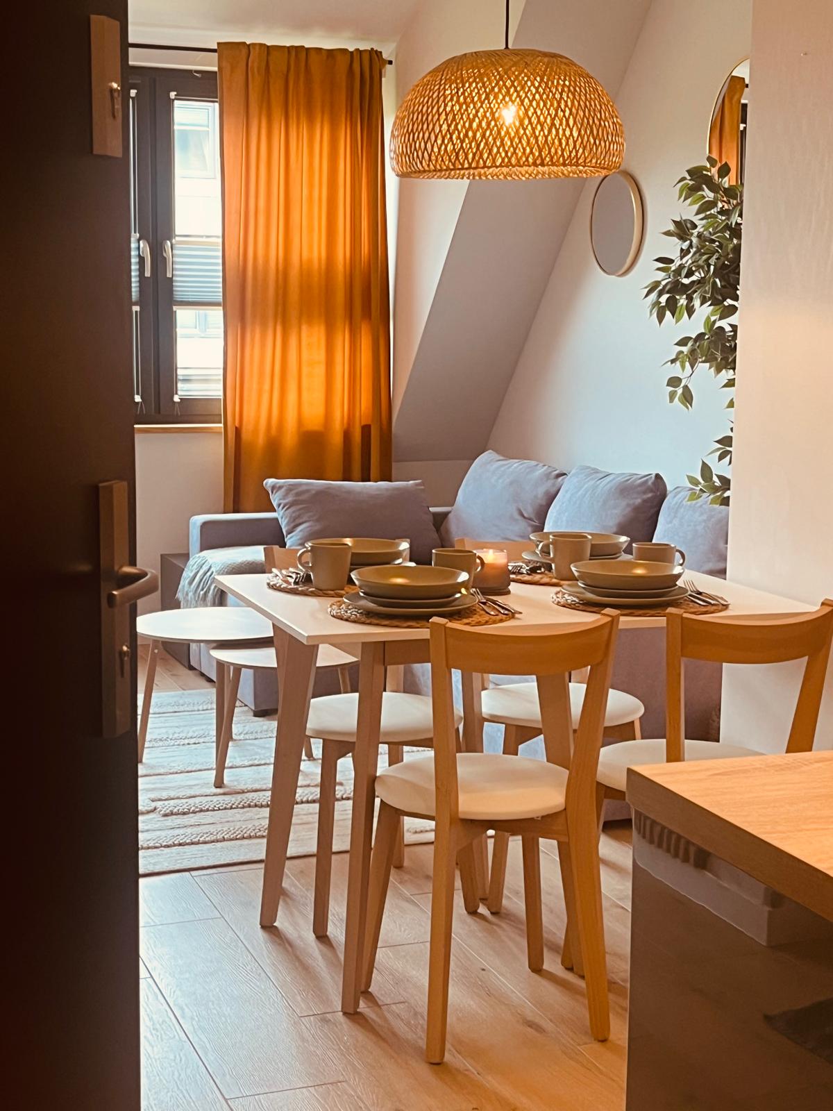 Apartament Kołobrzeg Lwowska 12B - jadalnia z salonem, eleganckie wnętrze z drewnianym stołem i pomarańczowymi zasłonami